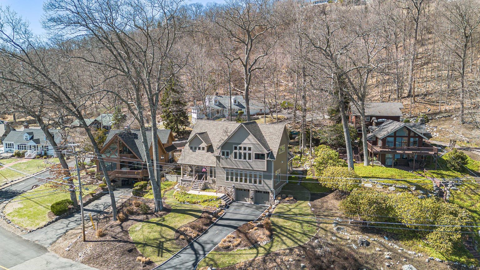 Aerial view of a home and neighboring properties beside a wooded hillside
